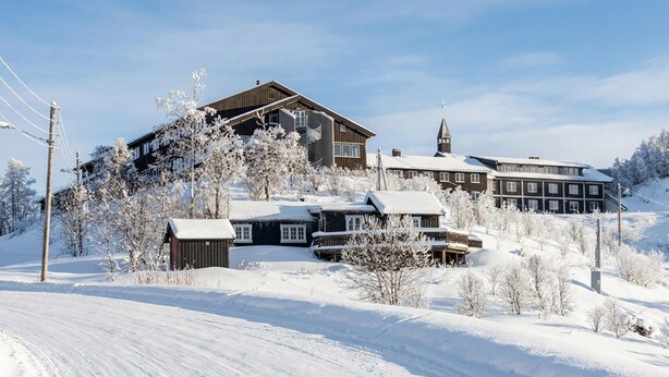 A snow-covered lodge with multiple buildings, including a main house and several smaller structures, surrounded by trees and a clear sky. - Herlig ferie nær Møsvatn (Rjukan)