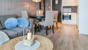 A cozy living room with a sofa, a coffee table with a candle, a dining area with chairs, and a kitchen with an oven. - Herlig ferie nær Møsvatn (Rjukan)