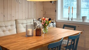 Una mesa de comedor de madera con un jarrón de flores y velas, un banco acolchado, y una ventana con vistas a árboles.