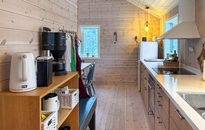 A compact kitchen with wooden walls, a coffee machine, a kettle, and a window with a view.