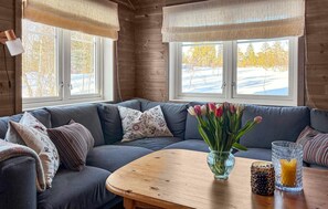 A cozy cabin interior with a grey sofa, a wooden coffee table, and a vase of tulips.