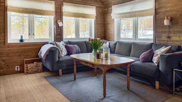Un interior de cabaña acogedor con un sofá gris, una mesa de centro de madera y un jarrón de flores.