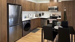 Une cuisine moderne avec des meubles en bois, des appareils en acier inoxydable, un four encastré et un coin repas avec des chaises noires.