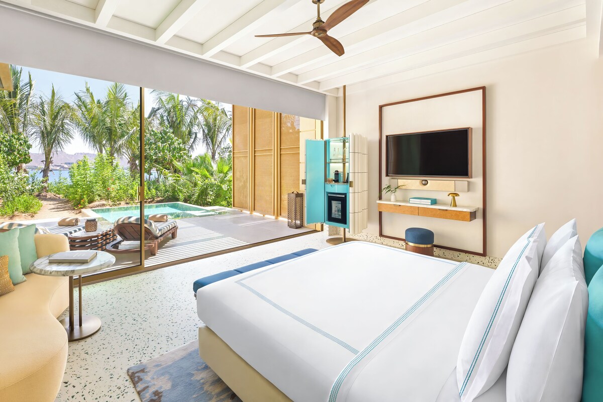 Un dormitorio moderno con una cama grande, un televisor y vistas a una piscina y zonas verdes.