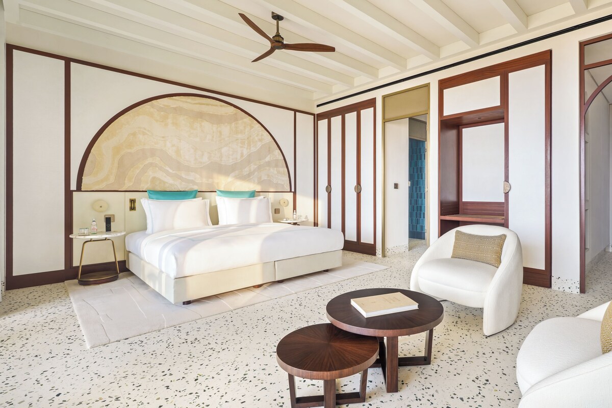 Habitación de hotel con cama, una silla, una mesita pequeña, ventilador de techo y un espejo grande.
