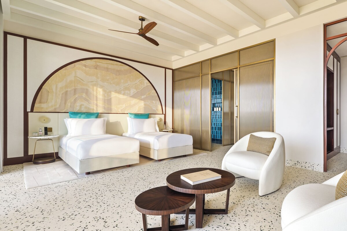 Una habitación de hotel con una cama grande, un sofá, una silla, una mesita y un ventilador de techo.