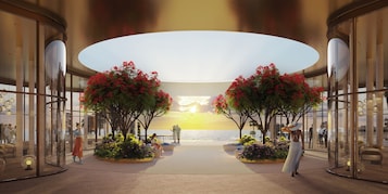 Um hall amplo com parede de vidro central que oferece vista para o mar, cercado por áreas de estar e plantas de interior.