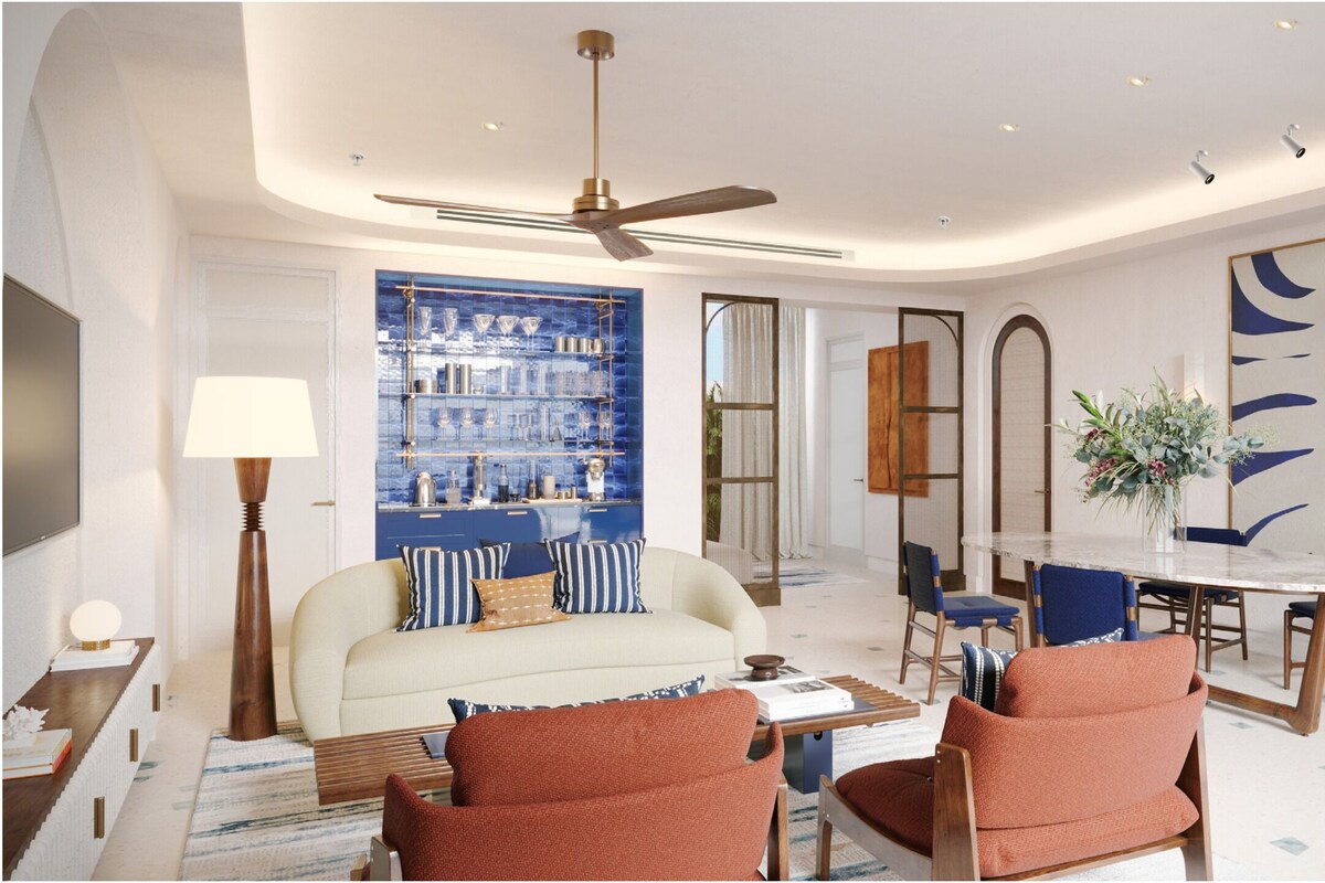 Ein modernes Wohnzimmer mit einer Couch, Sesseln, einem Couchtisch, einem Esstisch mit Stühlen, einem Deckenventilator und einer blauen Wand mit Regalen.