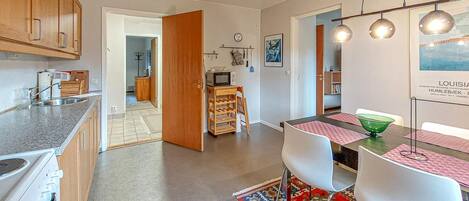 Une cuisine moderne dotée d’un four encastré, un coin repas avec une table et des chaises, et un couloir menant à une salle de bain.