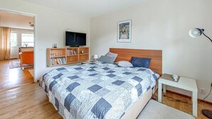 A bedroom with a large bed, a wooden headboard, a TV on a stand, a bookshelf, and a painting on the wall.