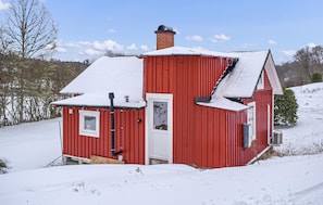 A red wooden house with a snow-covered roof, a chimney, and a small porch area.