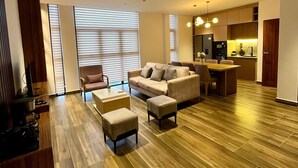 A modern living room with a sofa, ottoman, and a dining table. There is a kitchen area with a refrigerator and a sink. - Luxury Apartment in Colombo (Colombo)