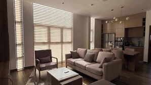 A modern living room with a sofa, armchairs, and ottomans. There is a kitchen area with a dining table and chairs. - Luxury Apartment in Colombo (Colombo)