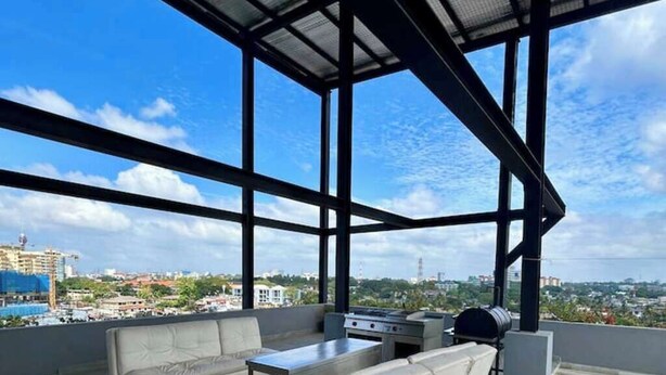 A rooftop terrace with a modern design, featuring a seating area with sofas and a table, a grill, and a view of the cityscape. - Luxury Apartment in Colombo (Colombo)