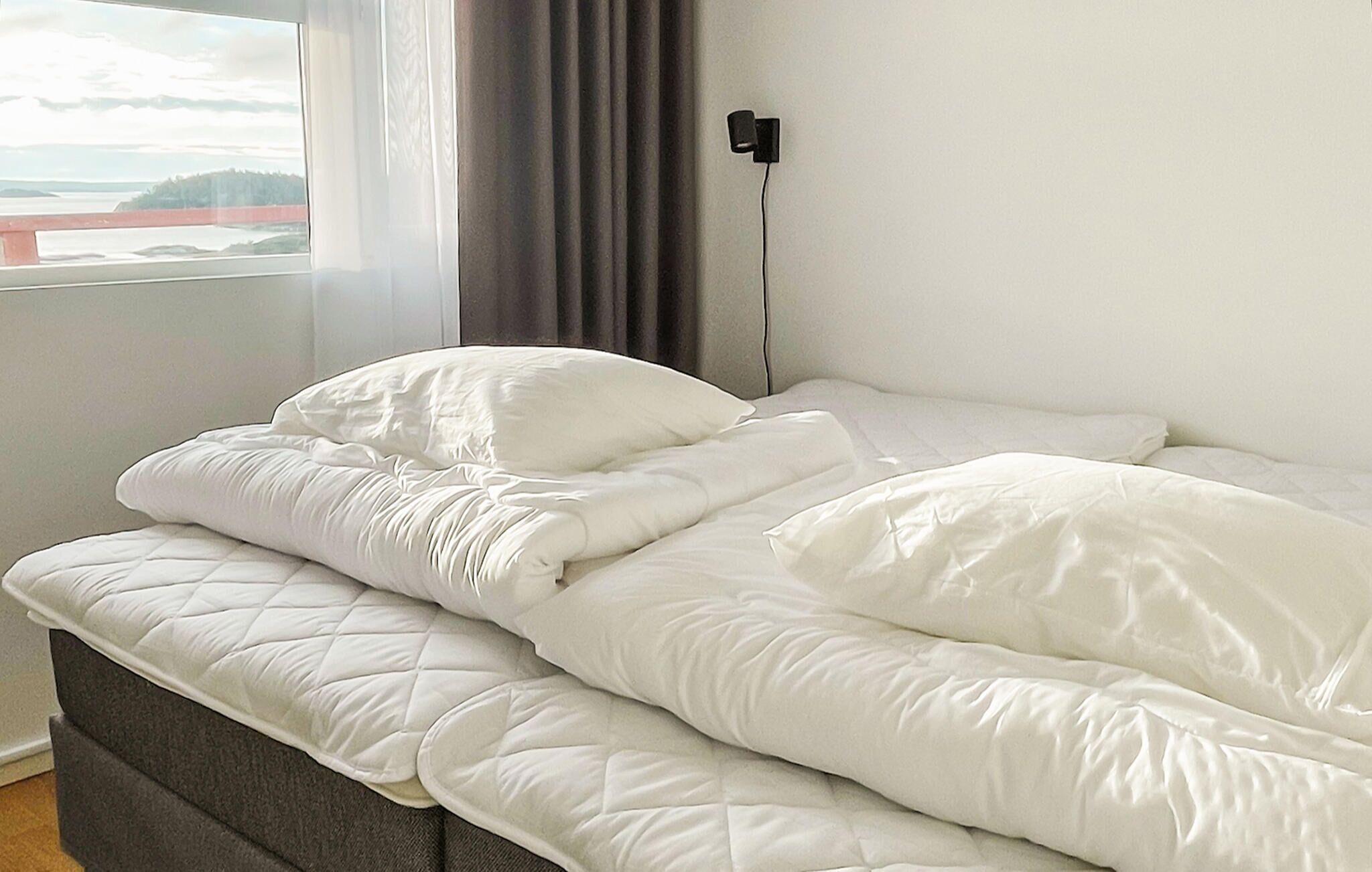 A neatly made bed with white bedding in a room with a window and a view of a bridge.