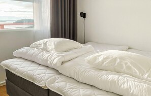 A neatly made bed with white bedding in a room with a window and a view of a bridge.