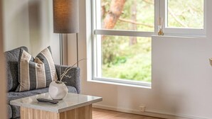 A living room with a grey sofa, a white vase with branches, and a remote control on a wooden coffee table.
