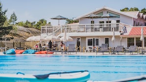 A pool area with lounge chairs and umbrellas, a wooden deck, and a building with a balcony. - 2 bedroom gorgeous apartment in Myggenäs (Myggenäs)