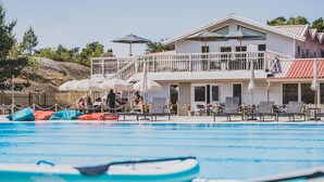 A pool area with lounge chairs and umbrellas, a wooden deck, and a building with a balcony. - 3 bedroom gorgeous apartment in Myggenäs (Myggenäs)