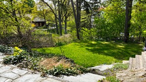 Un vialetto in pietra conduce a un prato curato, con una recinzione in legno e alberi sullo sfondo.