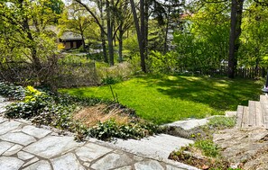 A stone pathway leading to a well-maintained lawn with a wooden fence and trees in the background.
