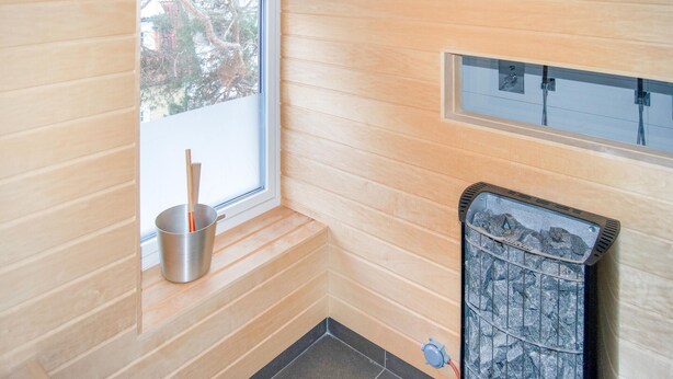 Una sauna con finestra, un catino di metallo e uno scaldasalviette in pietra.