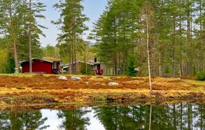 A cabin with a red exterior, surrounded by a forest and a body of water reflecting the trees. - 2 bedroom cozy home in Hagfors (Hagfors)