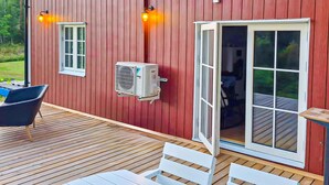 Ein rotes Holzgebäude mit Klimaanlage, einer Bank und einem Tisch auf einer Holzterrasse.