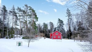 Eine rote Holzhütte in verschneitem Wald.