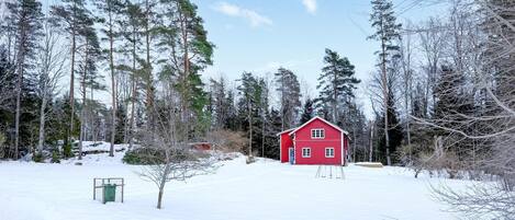 Punainen mökki lumisen metsän keskellä.