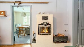 Ein gemütliches Wohnzimmer mit Kamin, eine Essecke mit Stühlen und Tisch, und eine Tür zu einem weiteren Raum.