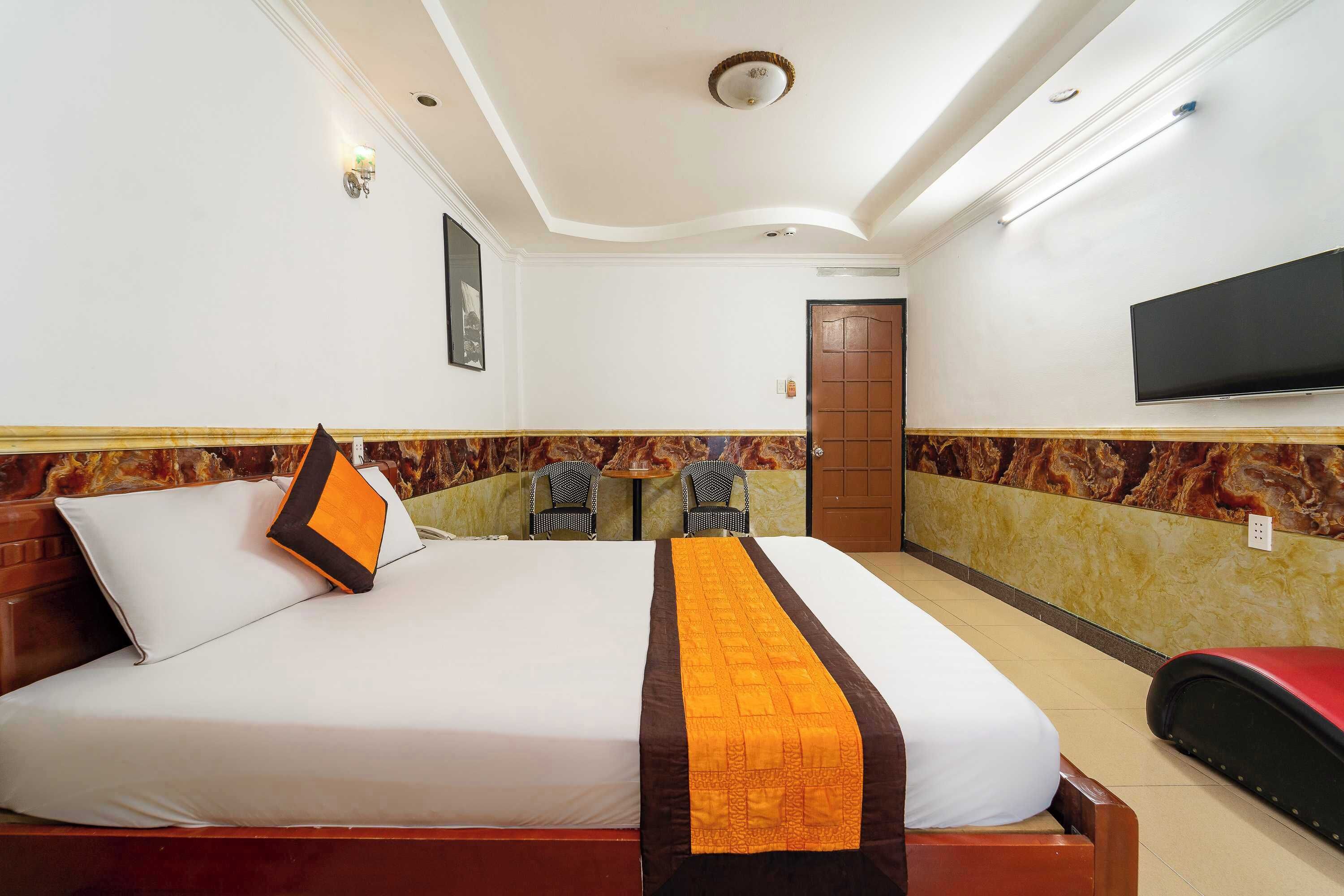 A hotel room with a large bed, a TV mounted on the wall, and a small table with chairs.