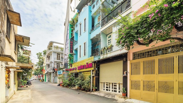 Une vue de rue avec un hôtel appelé « SONLAM » et un magasin fermé, dont la devanture est ornée d’une grille jaune.
