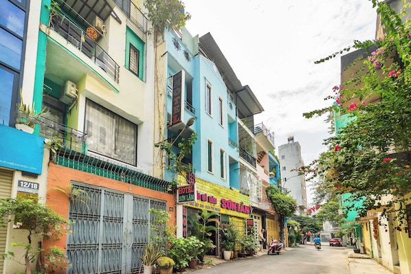 A narrow street lined with colorful buildings, including a hotel with a balcony and a sign that reads "HOTEL SON LAM".