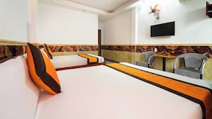 Une chambre d’hôtel avec deux lits, une télévision, un climatiseur et un ventilateur au mur.