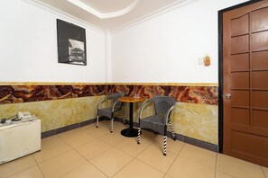 A room with two black and white patterned chairs around a small round table, a white desk with a telephone, and a door with a brown panel.