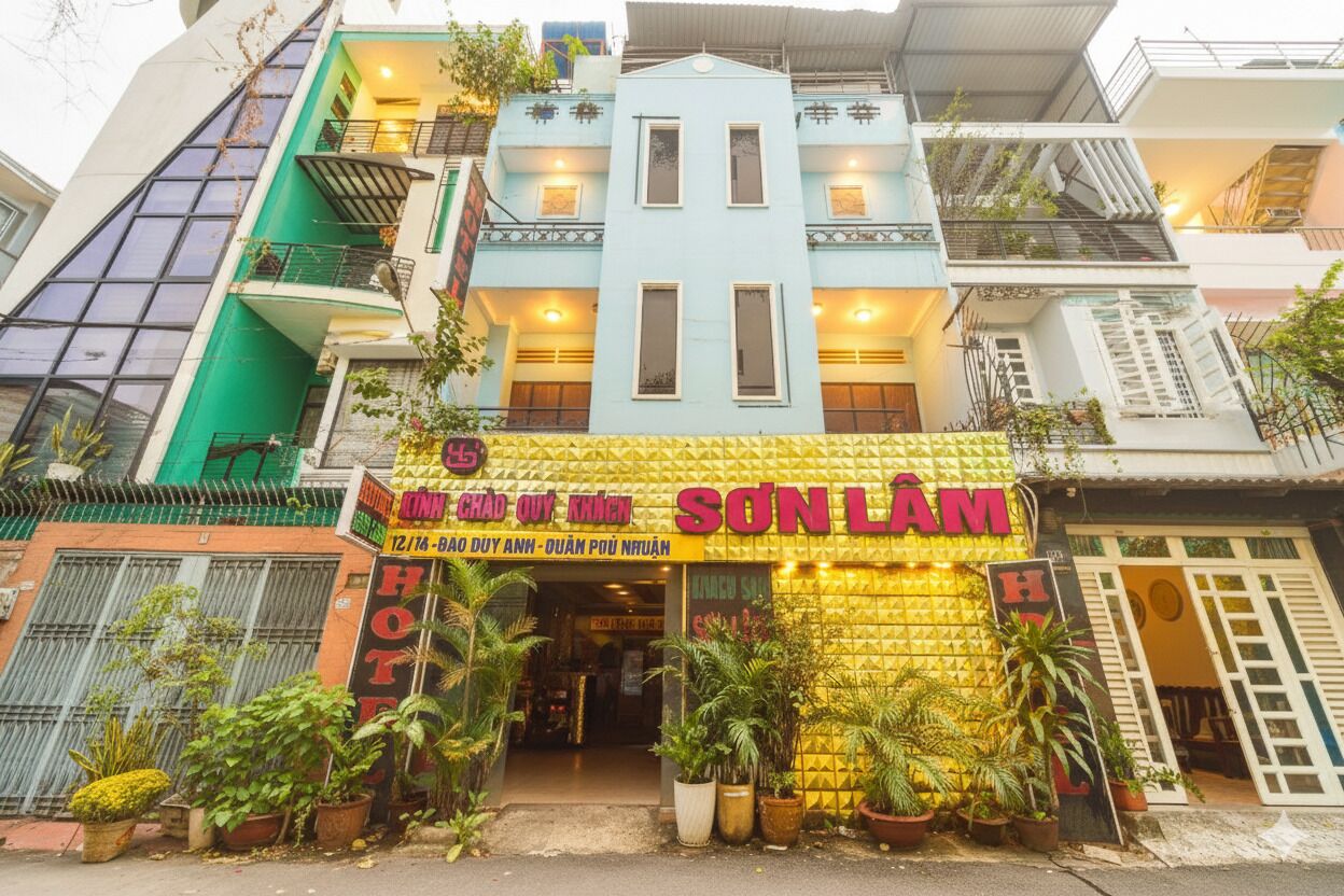 A hotel with a yellow facade, multiple balconies, and potted plants in front.