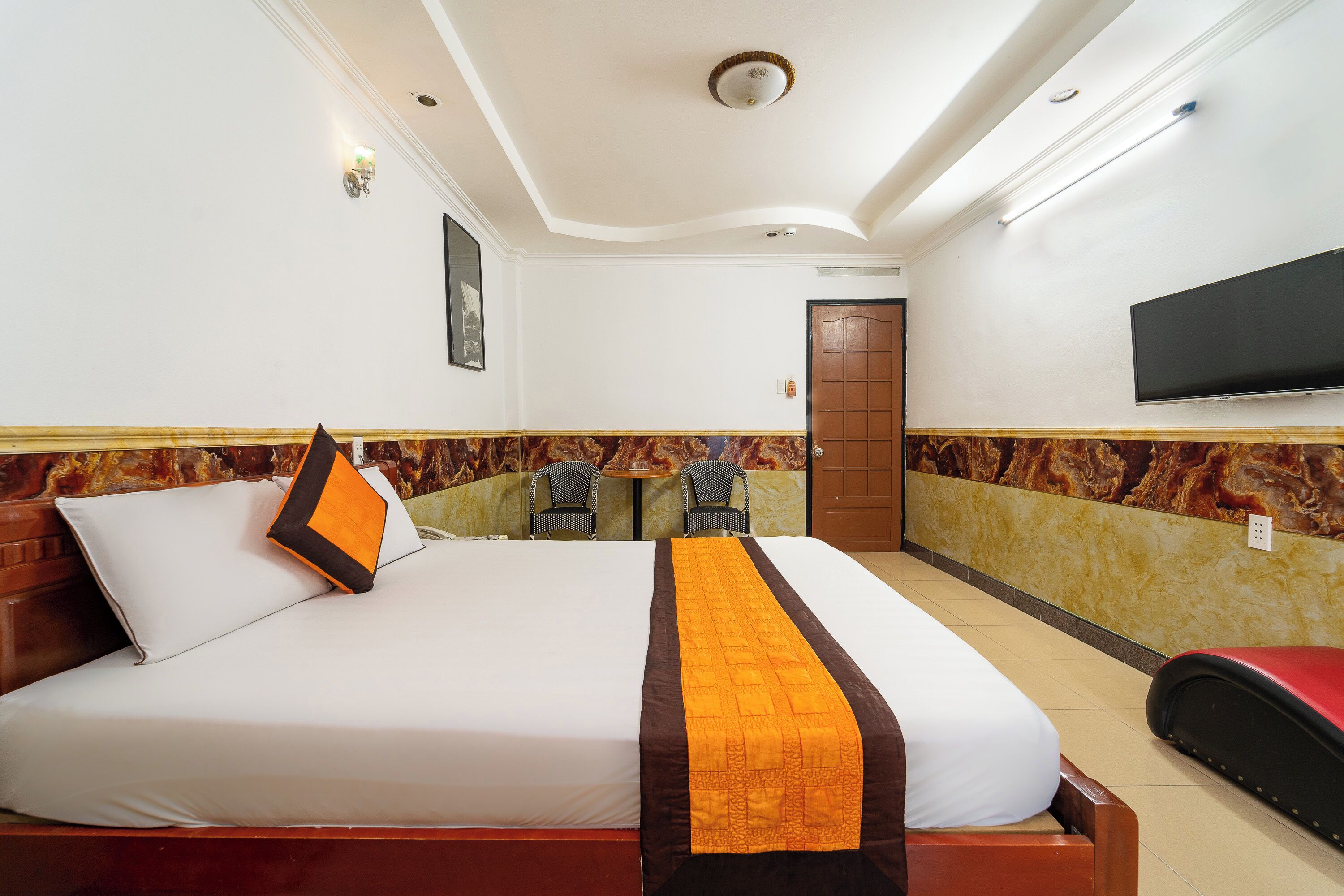 Habitación de hotel con una cama grande, un televisor montado en la pared y una pequeña mesa con sillas.