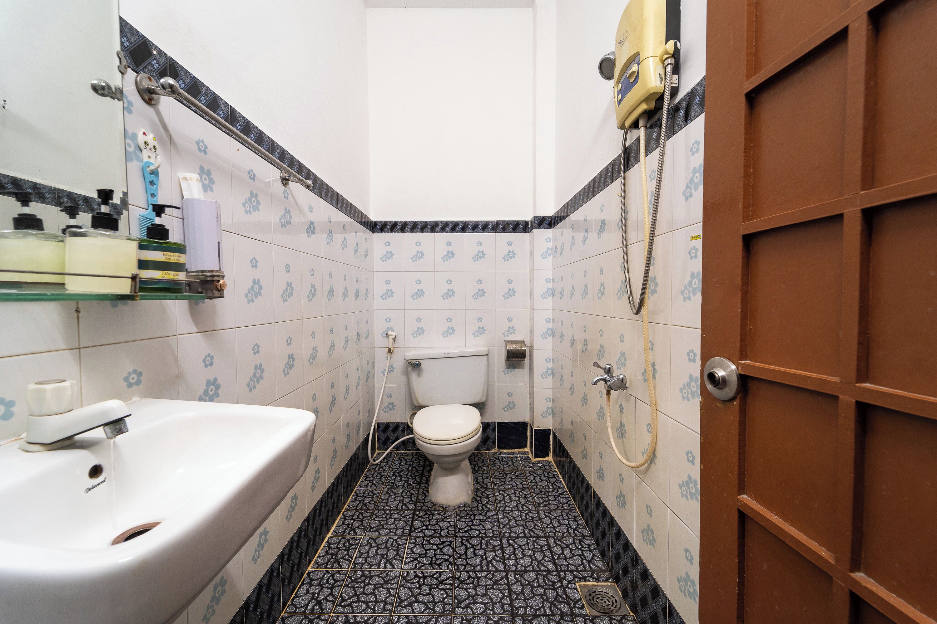Un baño con lavamanos, inodoro y ducha blancos. Hay artículos de aseo en un estante y un perchero.