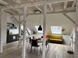 Ein Loft-Zimmer mit Essbereich, einem gelben Sofa und einer Küche im Hintergrund.