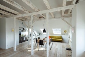 A spacious loft with exposed wooden beams, a dining area, a yellow sofa, and a kitchen in the background. - Loft on the top floor of the Häselburg with far-reaching views (Gera)