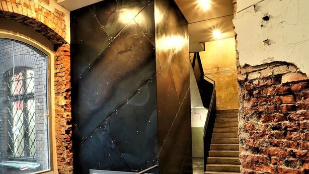 Uma escadaria moderna com corrimão de metal preto, paredes de tijolo e uma janela de vidro à esquerda.