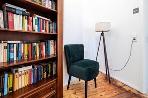 Ein Zimmer mit einem hölzernen Bücherregal voller Bücher, einem grünen Sessel und einer Stehlampe.