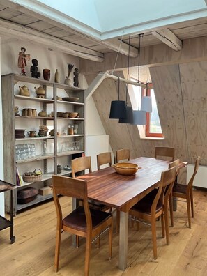 Ein Essbereich mit Holztisch und -stühlen, einem Bücherregal mit Keramik und einer schrägen Decke mit Dachfenster.