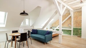 A modern loft bedroom with a sloped ceiling, a wooden dining table with chairs, a teal sofa, and a hanging pendant light. - Central & bright - penthouse 23 in the Häselburg (Gera)