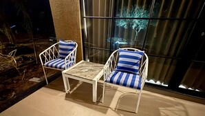 Two white chairs with blue and white striped cushions and a small white table on a tiled floor, positioned in front of a large window with a view of trees and a building. - Jalsa Jawai (Bali)