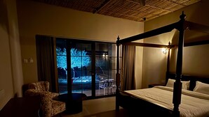 A bedroom with a four-poster bed, a chair, and a large window with a view of trees. - Jalsa Jawai (Bali)