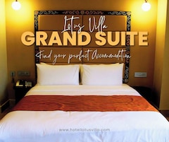 A hotel room with a large bed, two bedside tables, a nightstand, and a wall-mounted light fixture. The room has a warm color scheme and a decorative headboard.