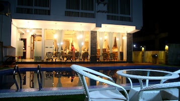 A hotel exterior at night with a pool, outdoor seating, and a well-lit entrance.