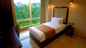Quarto de hotel com uma cama grande, uma mesinha de cabeceira, uma cadeira e vista para o verde pela janela.